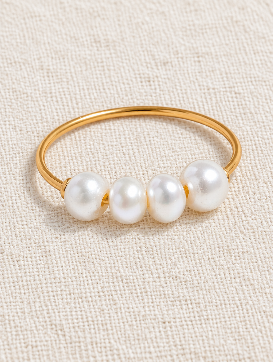 Gold thin band ring with four pearls resting on a soft textured surface
