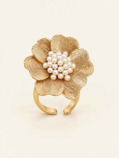 Gold textured flower ring with pearl centre on a neutral background