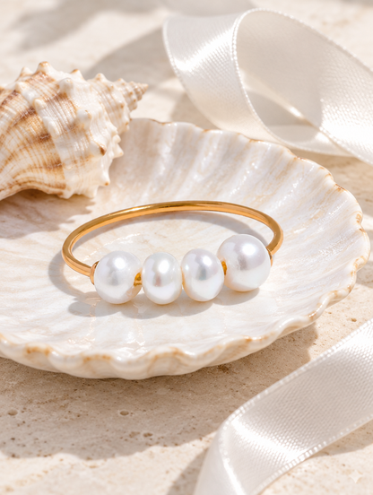 Gold thin band ring with four pearls in a small dish with styling props