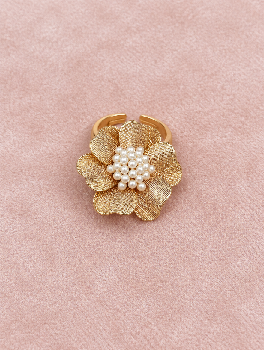 Gold textured flower ring with pearl centre resting on a soft textured surface