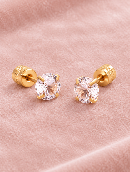 Gold twist-back stud earrings with pink stone lying flat on a soft styled surface