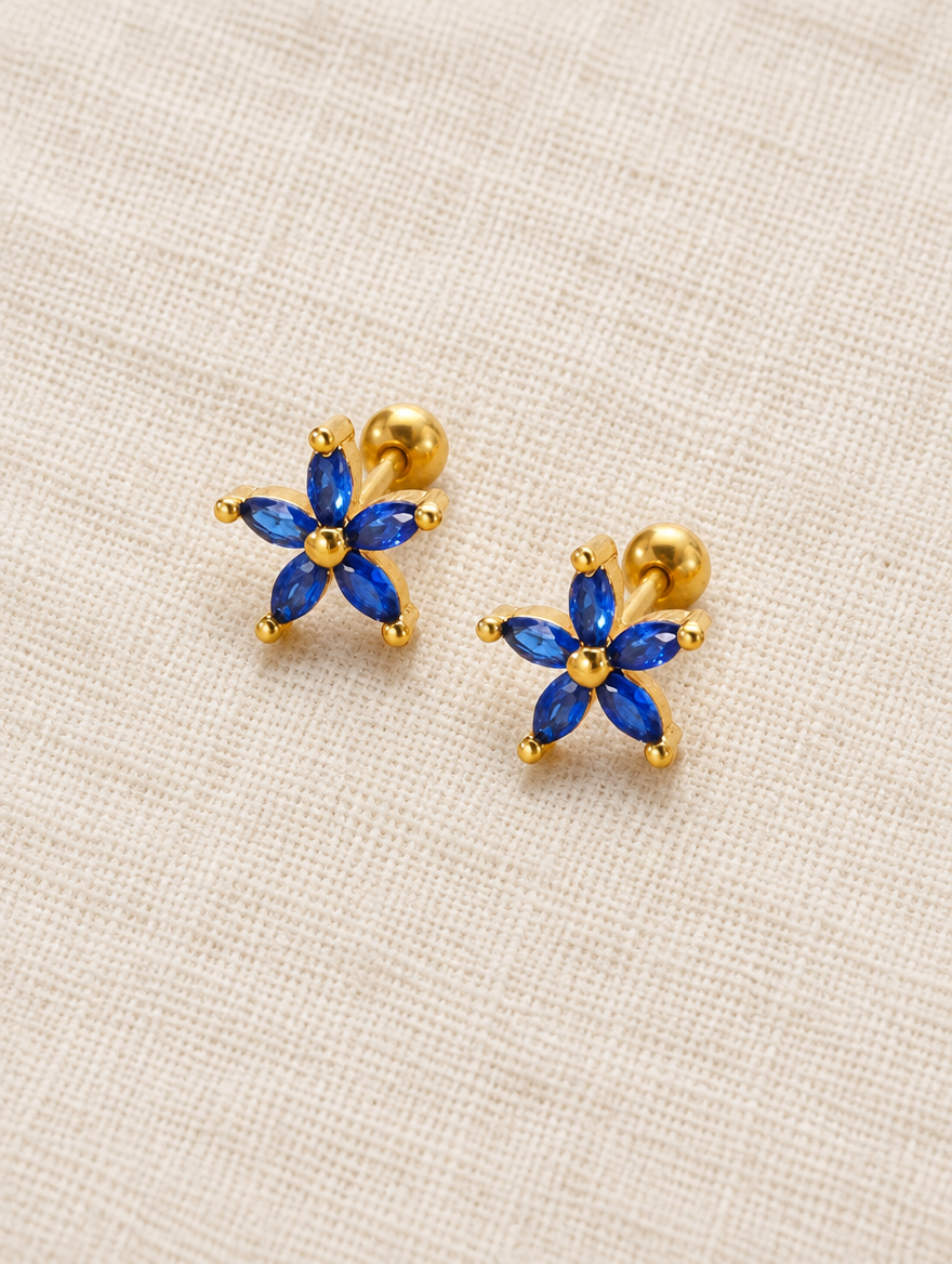 Gold blue flower stud earrings lying flat on a soft styled surface