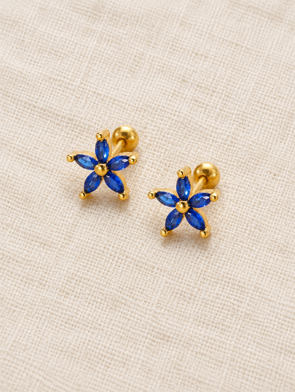 Gold blue flower stud earrings lying flat on a soft styled surface