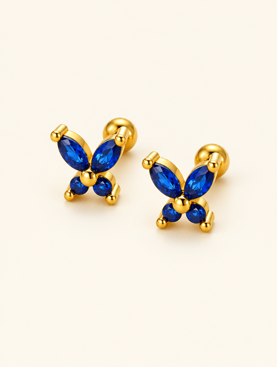 Pair of gold blue butterfly stud earrings on a warm off-white background