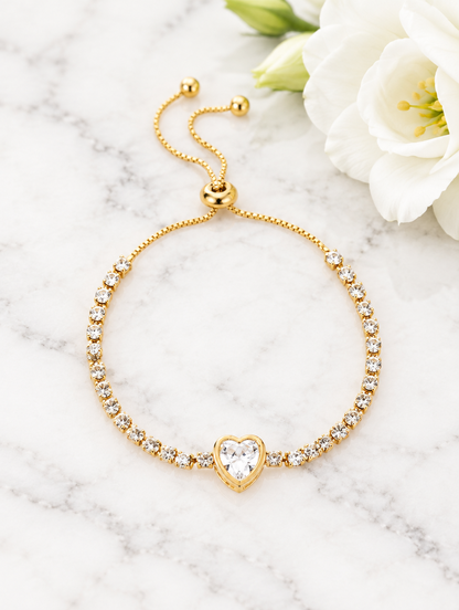 Gold heart tennis bracelet beside a white flower on marble