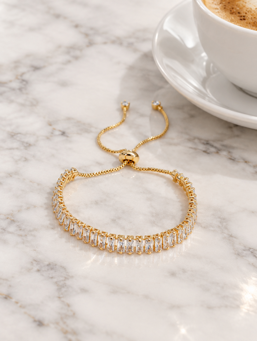 Gold baguette tennis bracelet beside a coffee cup on marble