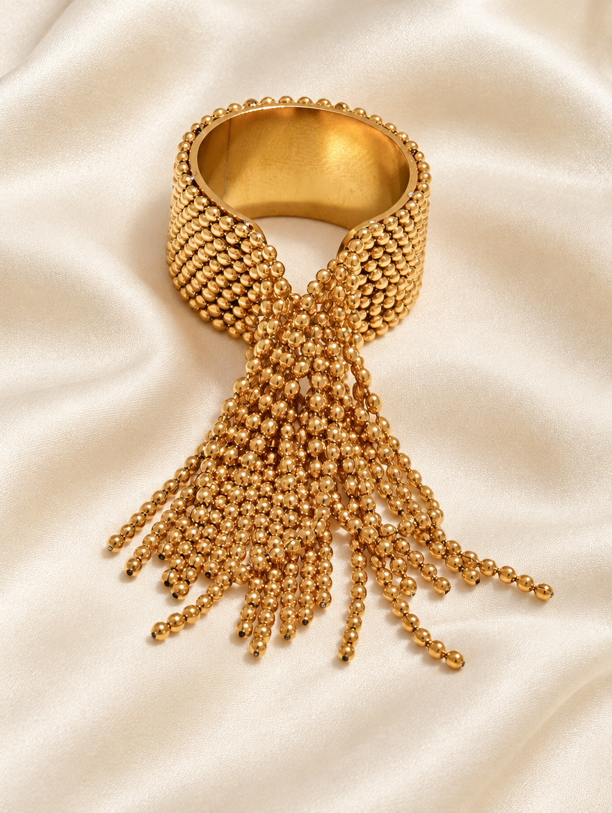 Gold ball chain tassel ring resting on a soft textured surface