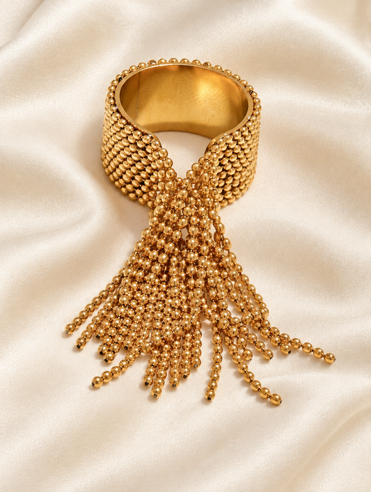 Gold ball chain tassel ring resting on a soft textured surface