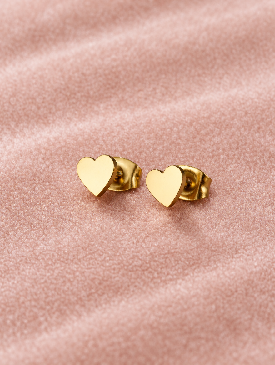 Gold heart stud earrings lying flat on a soft styled surface