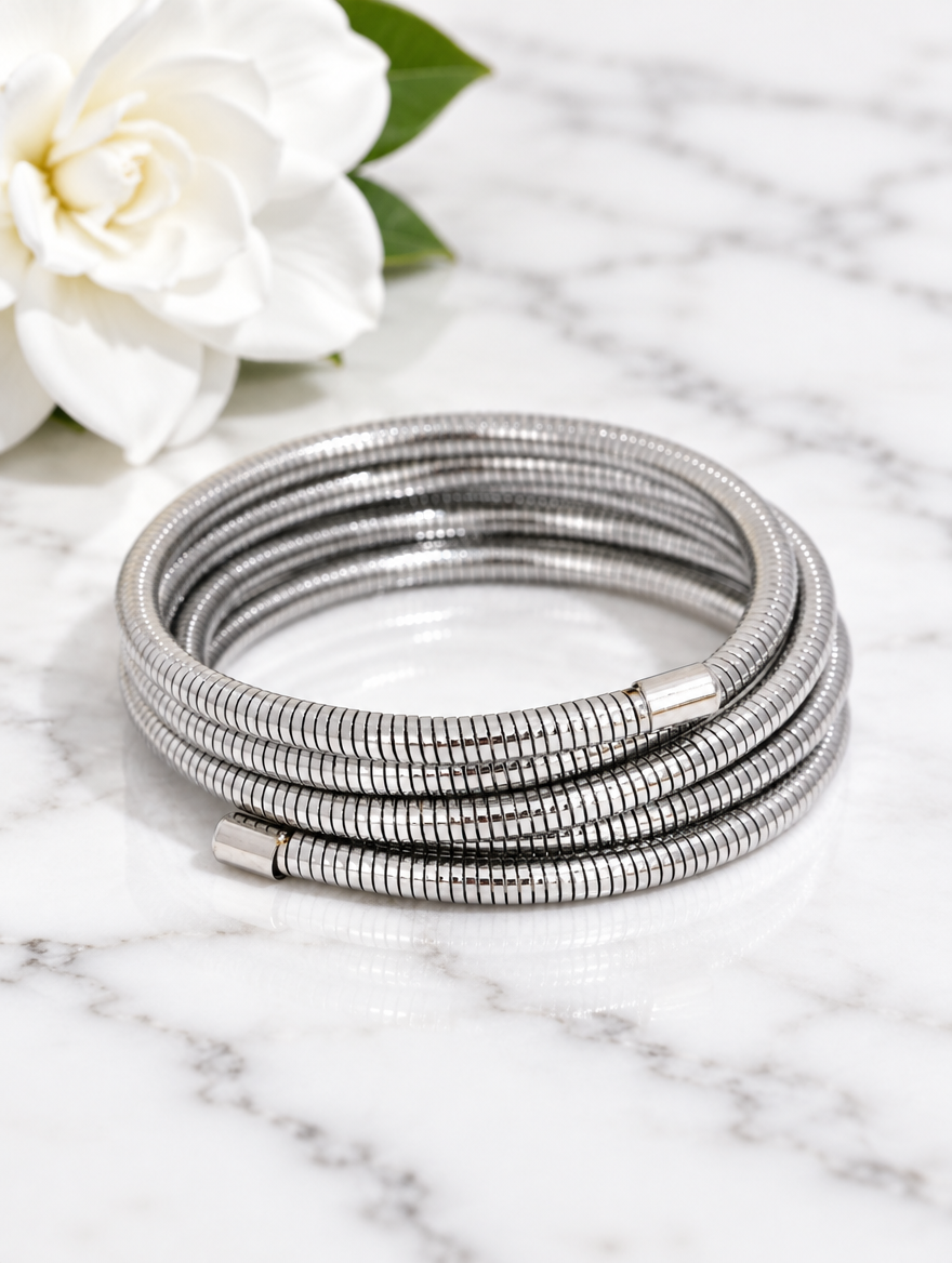 Silver wrap bracelet beside a white flower on marble