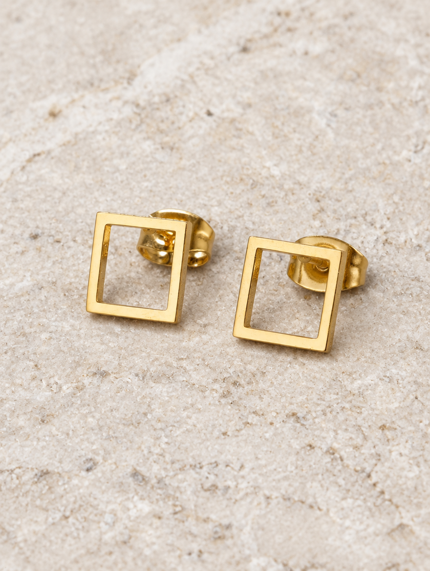 Gold open square stud earrings lying flat on a soft styled surface