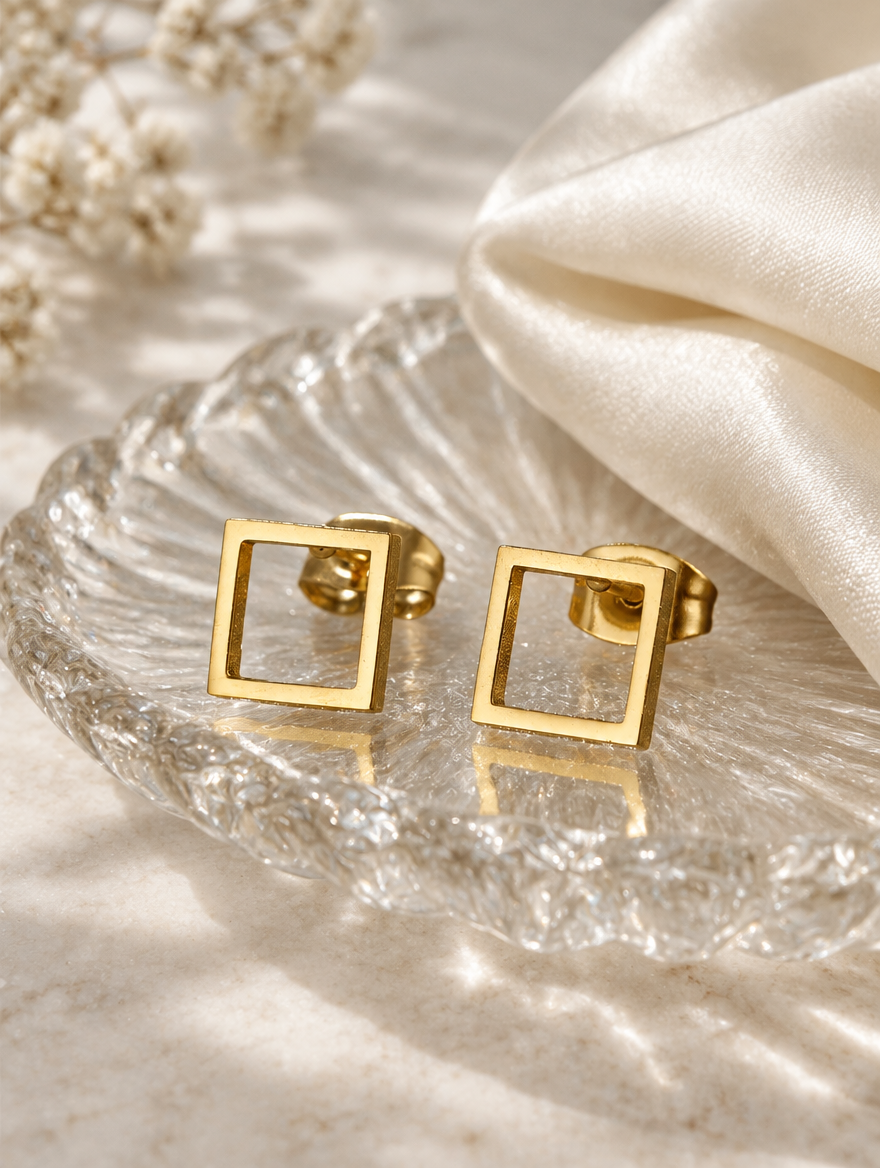 Gold open square stud earrings in a styled still life with props