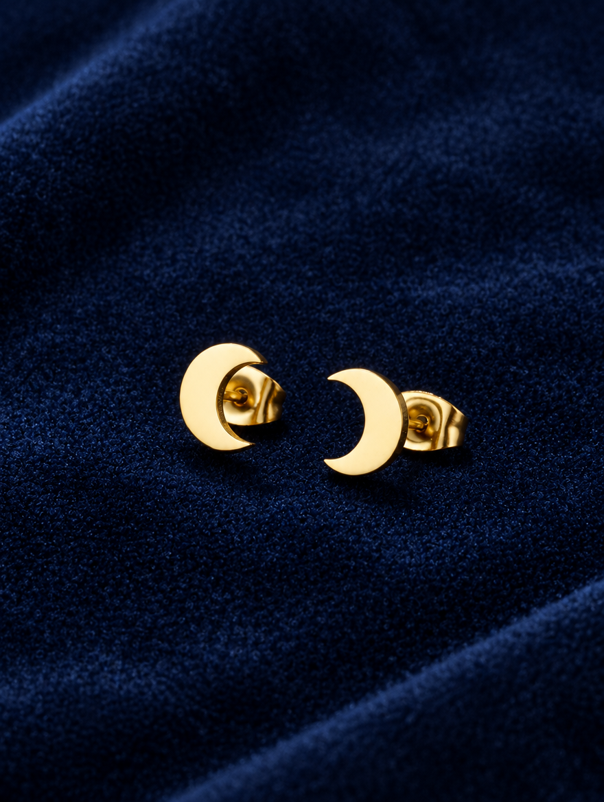 Gold crescent moon stud earrings lying flat on a soft styled surface