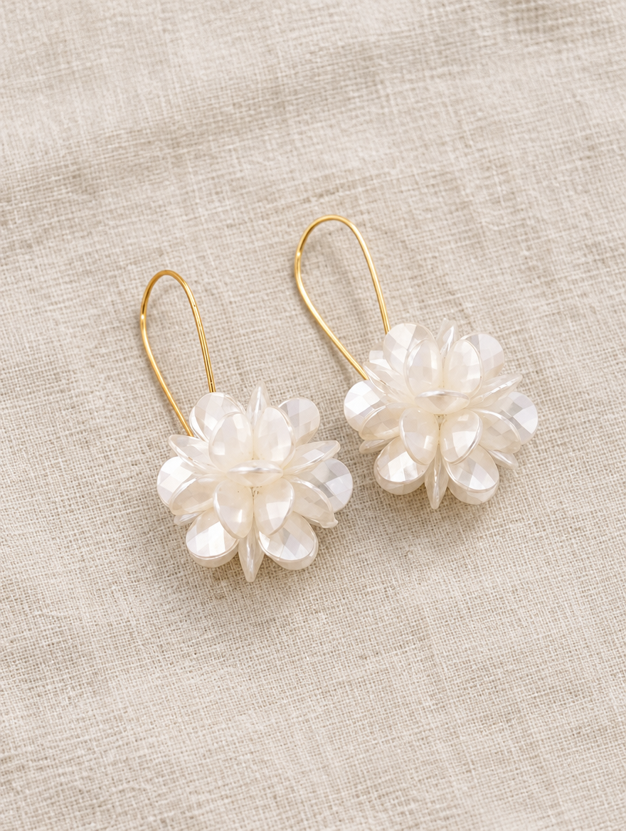 Pearl-look petal ball hook earrings lying flat on a soft styled surface