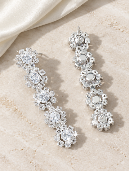 Silver floral crystal long drop earrings lying flat on a soft styled surface