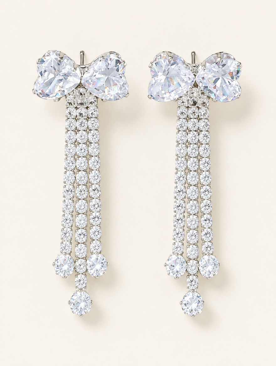 Pair of silver crystal bow tassel drop earrings on a warm off-white background