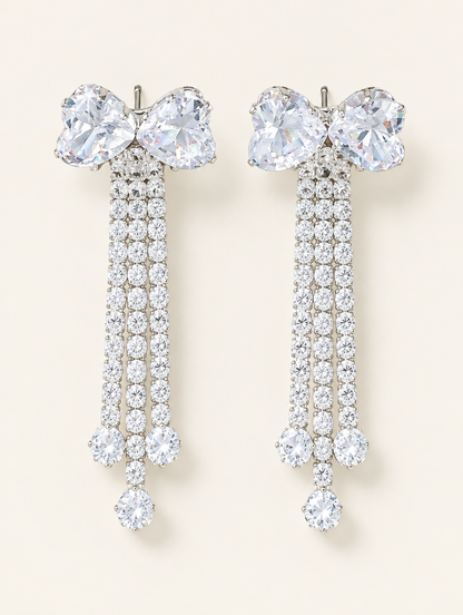Pair of silver crystal bow tassel drop earrings on a warm off-white background