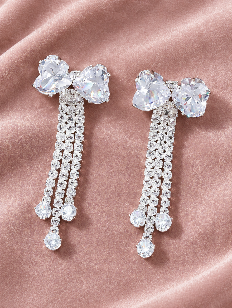 Silver crystal bow tassel drop earrings lying flat on a soft styled surface