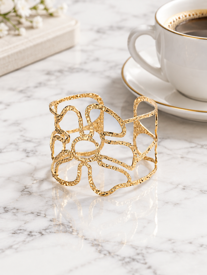 Gold wavy openwork cuff beside a coffee cup on marble
