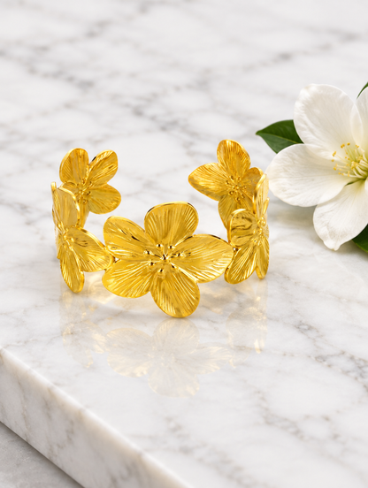 Gold flower cuff bracelet beside a white flower on marble