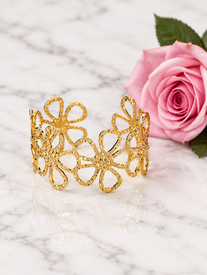 Gold outline flower cuff beside a pink rose on marble