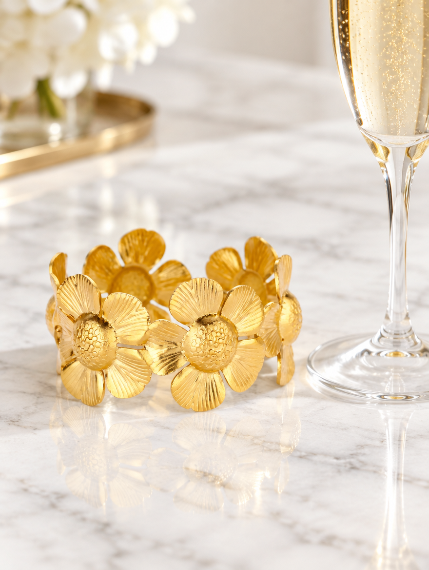 Gold daisy band bracelet beside a champagne flute on marble