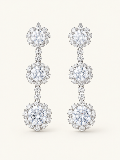 Pair of silver three-flower crystal drop earrings on a warm off-white background