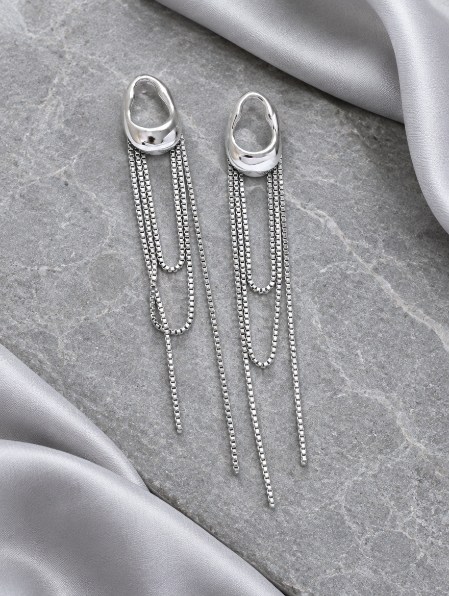 Silver chain tassel drop earrings with pearl-look bead lying flat on a soft styled surface