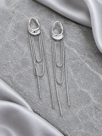 Silver chain tassel drop earrings with pearl-look bead lying flat on a soft styled surface