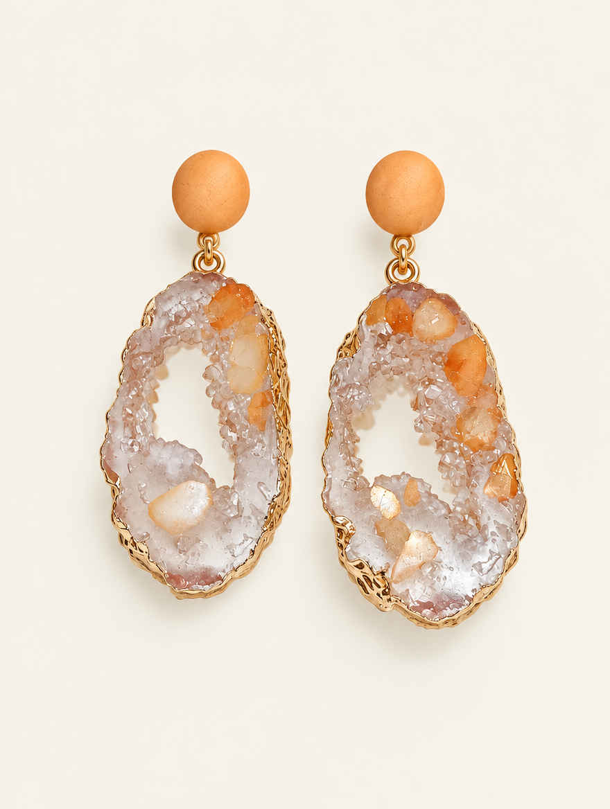 Pair of orange stone-look drop earrings with gold-tone edge on a warm off-white background