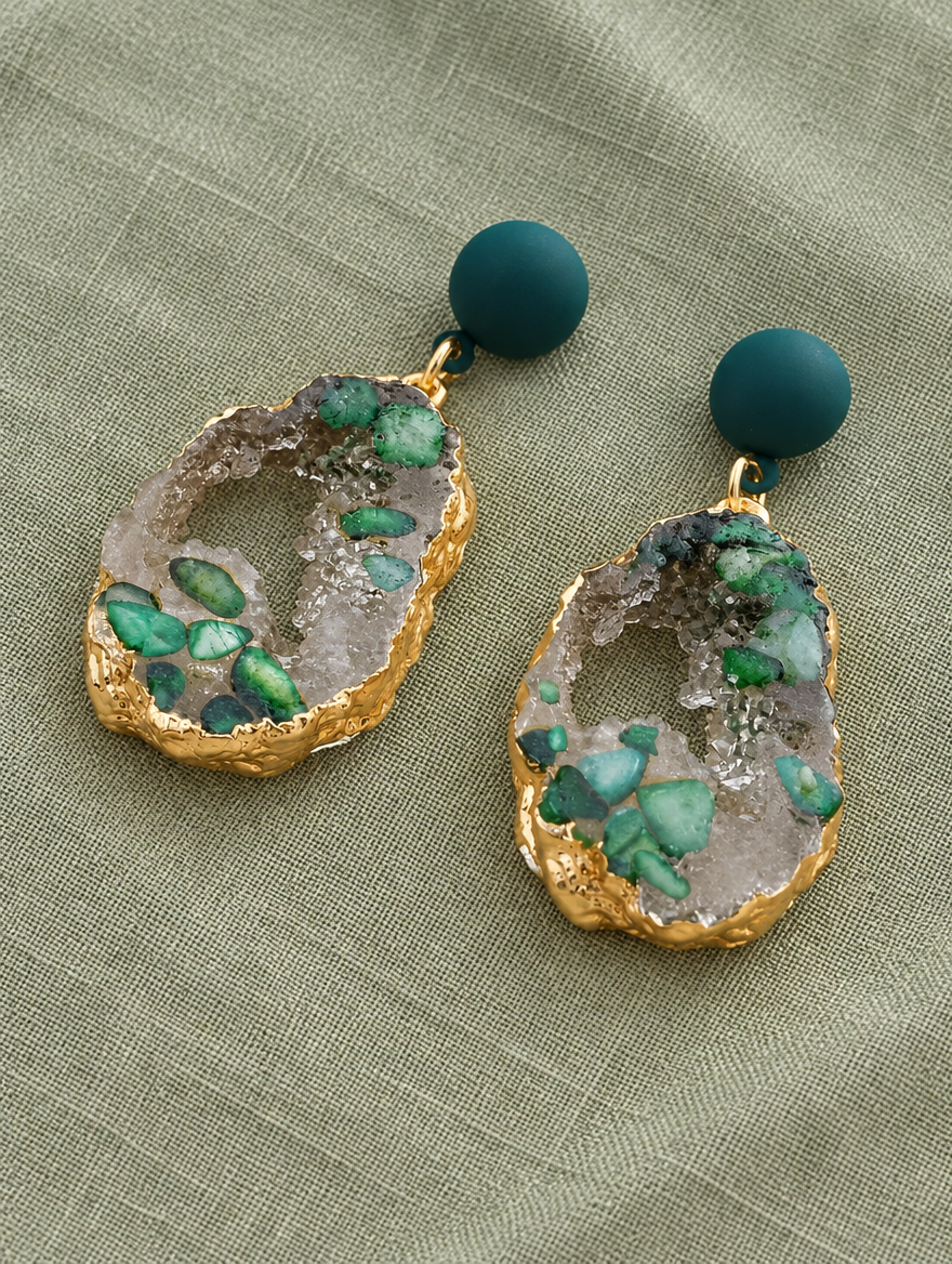 Green stone-look drop earrings with gold-tone edge lying flat on a soft styled surface