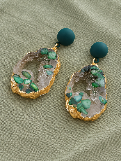 Green stone-look drop earrings with gold-tone edge lying flat on a soft styled surface