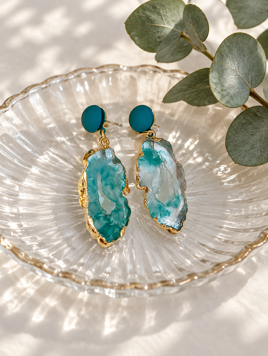 Teal stone-look drop earrings with gold-tone edge in a styled still life with props