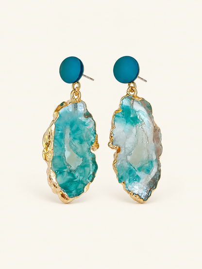 Pair of teal stone-look drop earrings with gold-tone edge on a warm off-white background