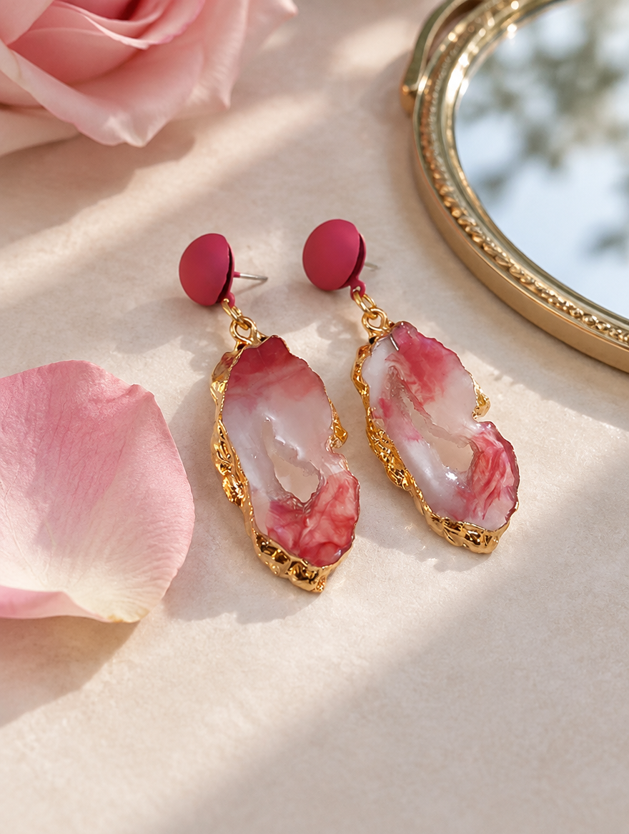 Pink stone-look drop earrings with gold-tone edge in a styled still life with props