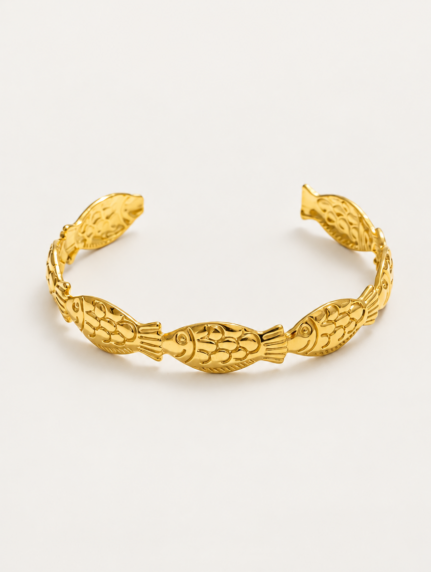 Gold fish open cuff bracelet on a neutral background
