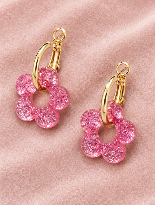 Gold-tone flower huggie hoop earrings lying flat on a soft styled surface