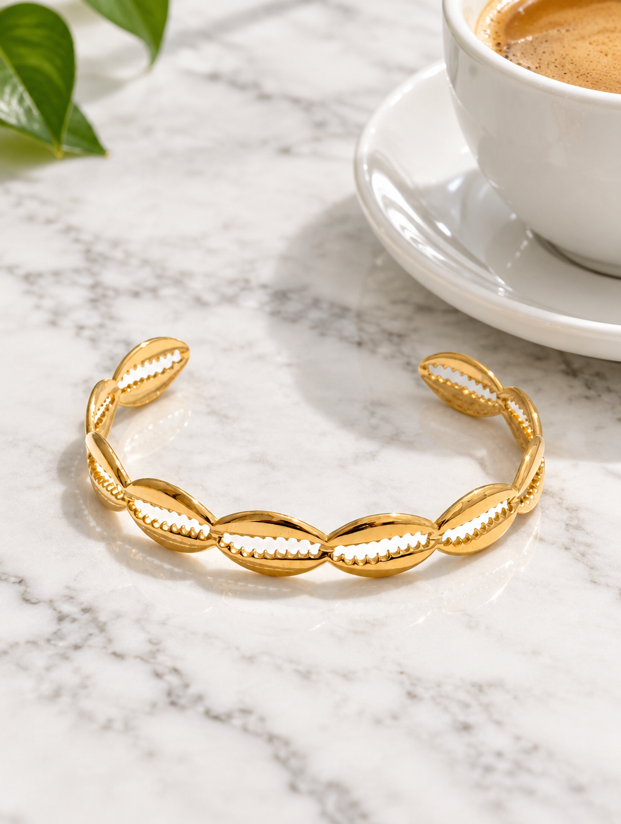 Gold hollow shell cuff bracelet beside a coffee cup on marble