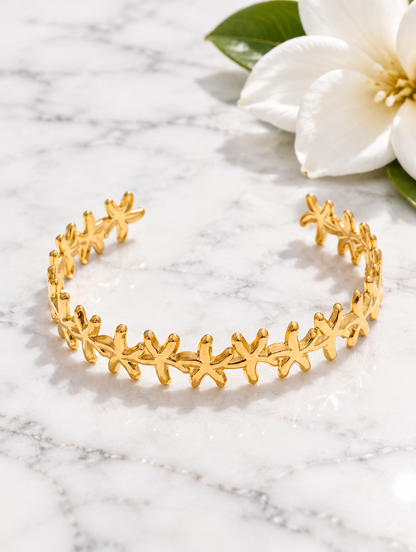 Gold starfish cuff bracelet beside a white flower on marble