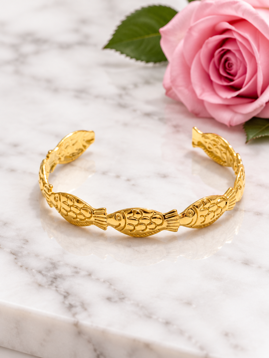 Gold fish cuff bracelet beside a pink rose on marble
