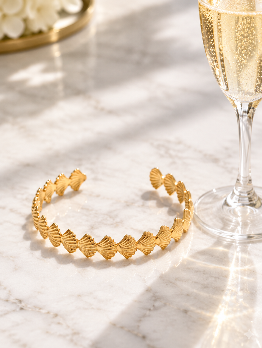 Gold scallop shell cuff bracelet beside a champagne flute on marble