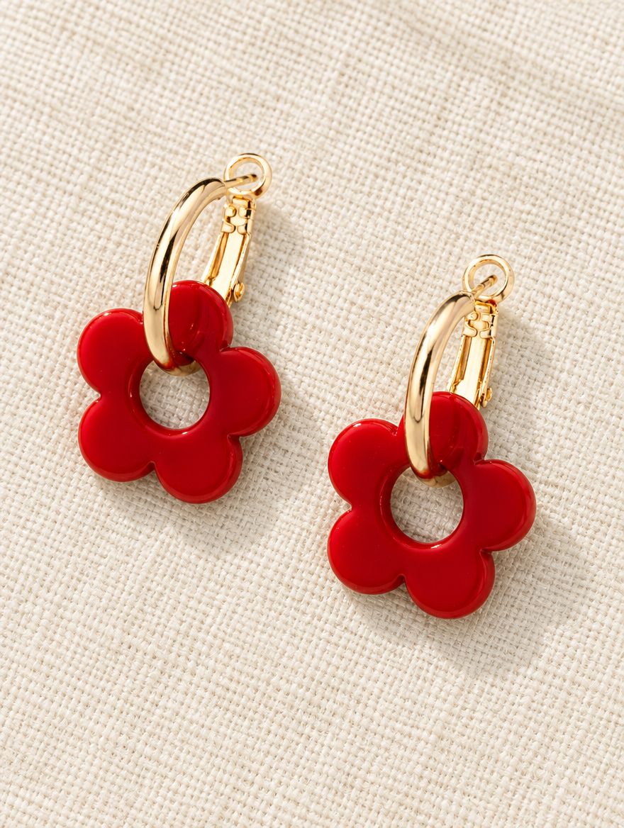 Gold-tone flower huggie hoop earrings lying flat on a soft styled surface