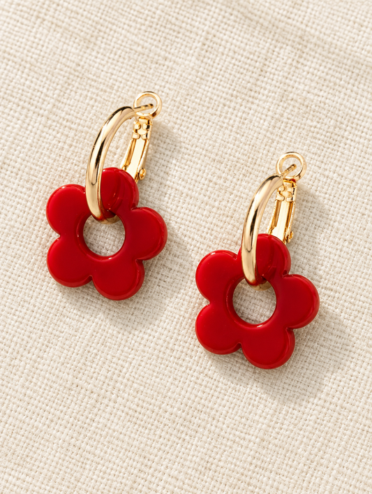 Gold-tone flower huggie hoop earrings lying flat on a soft styled surface