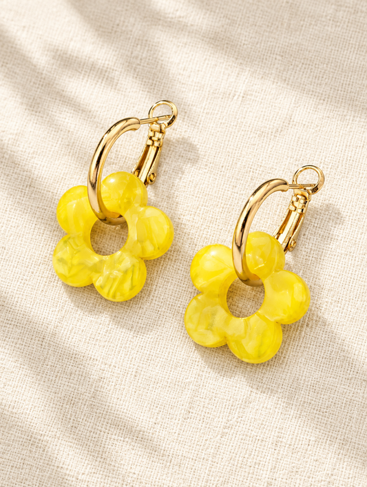 Gold-tone flower huggie hoop earrings lying flat on a soft styled surface