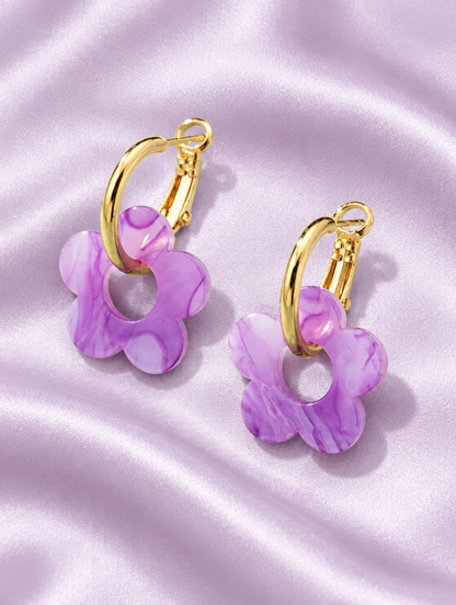 Gold-tone flower huggie hoop earrings lying flat on a soft styled surface