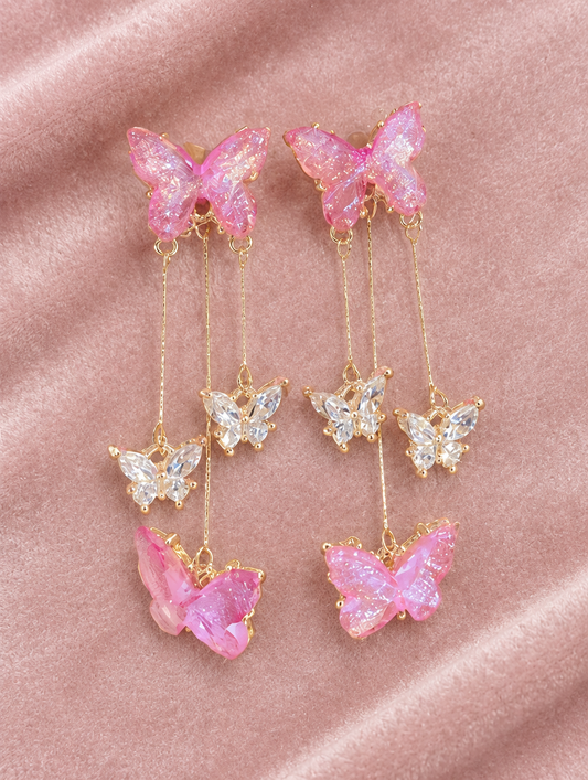 Pink butterfly tassel drop earrings lying flat on a soft styled surface