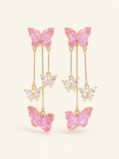 Pair of pink butterfly tassel drop earrings on a warm off-white background