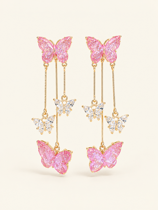 Pair of pink butterfly tassel drop earrings on a warm off-white background