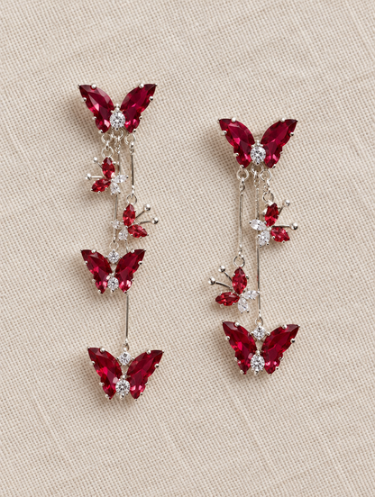Red butterfly tassel drop earrings lying flat on a soft styled surface