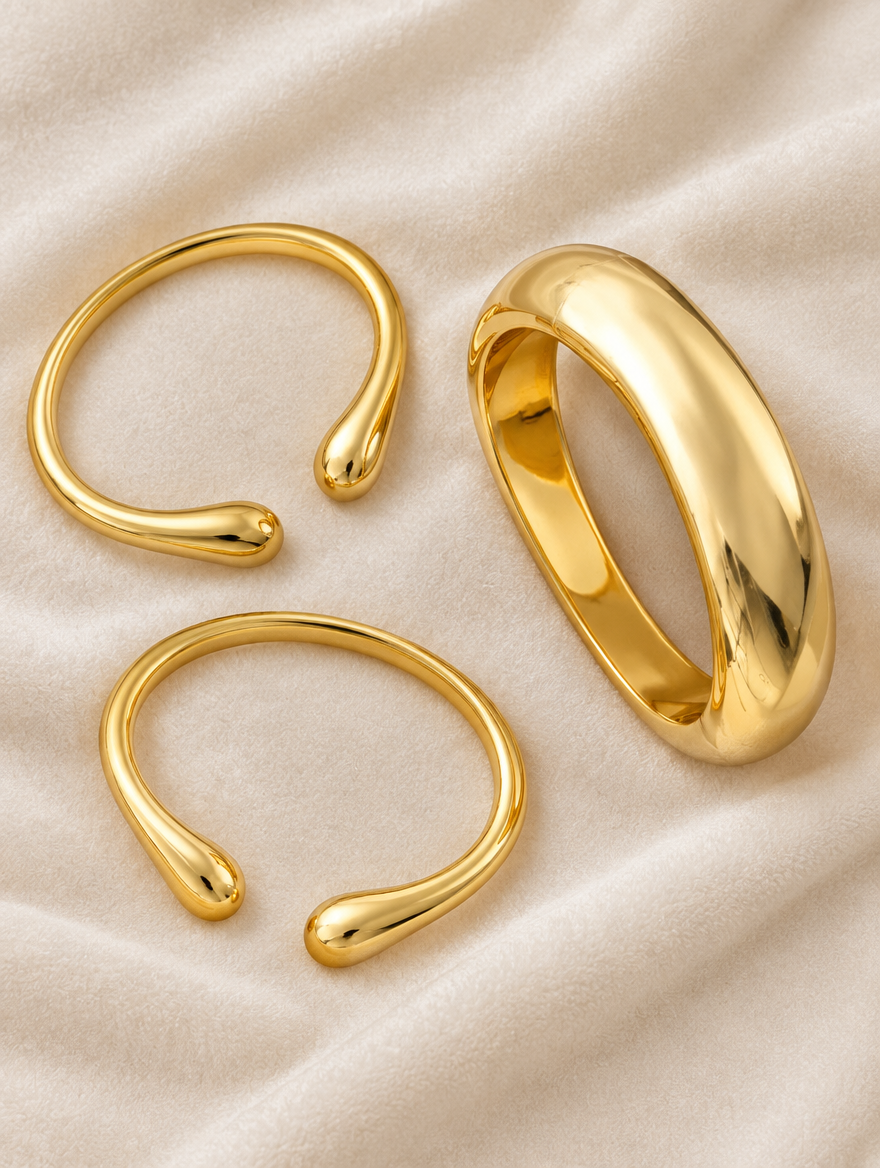 Three gold-tone open bangles laid out on cream velvet